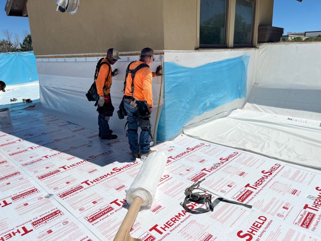 roofing crew in orange and safety harnesses installing single ply pvc roofing